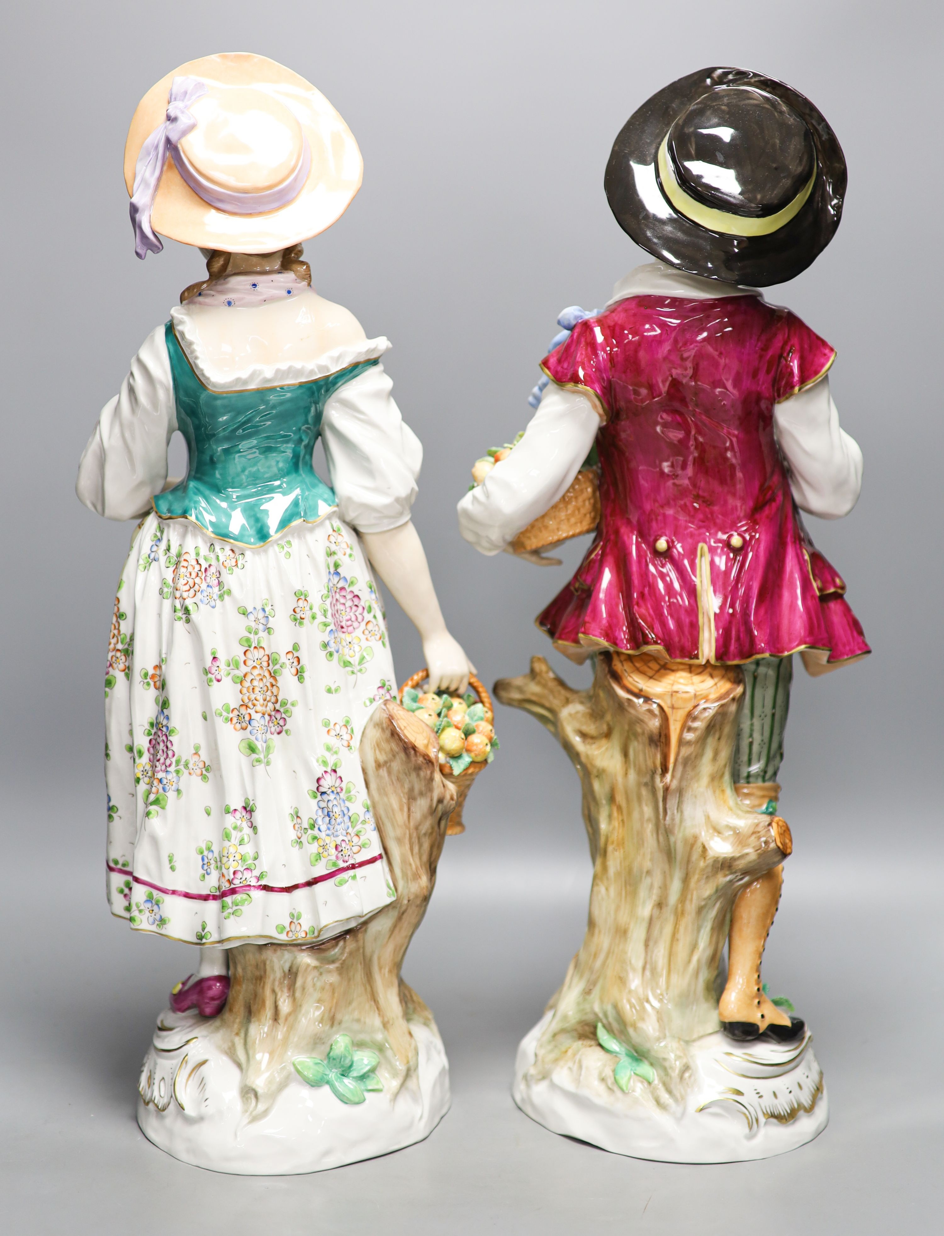 A pair of large Sitzendorf porcelain figures of a maid and a gallant, carrying baskets of fruit 52cm